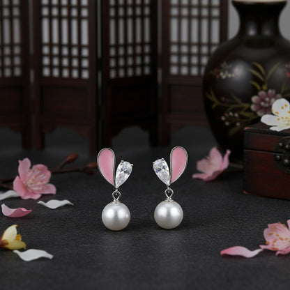 Pair of earrings with pink heart-shaped elements and pearl drops on a dark surface with floral decorations.