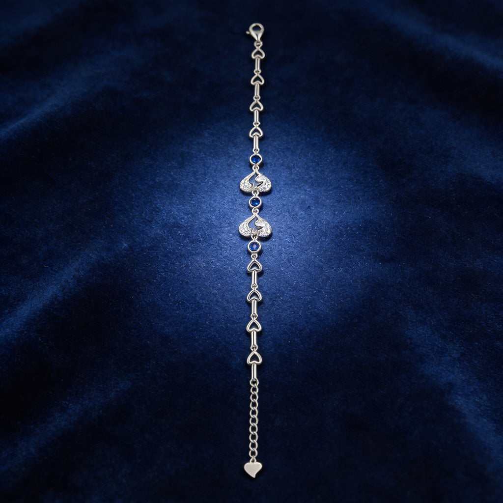 Silver bracelet with heart-shaped charms on a dark blue fabric background