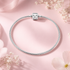 Silver bracelet with a matching charm on a pink background with flowers