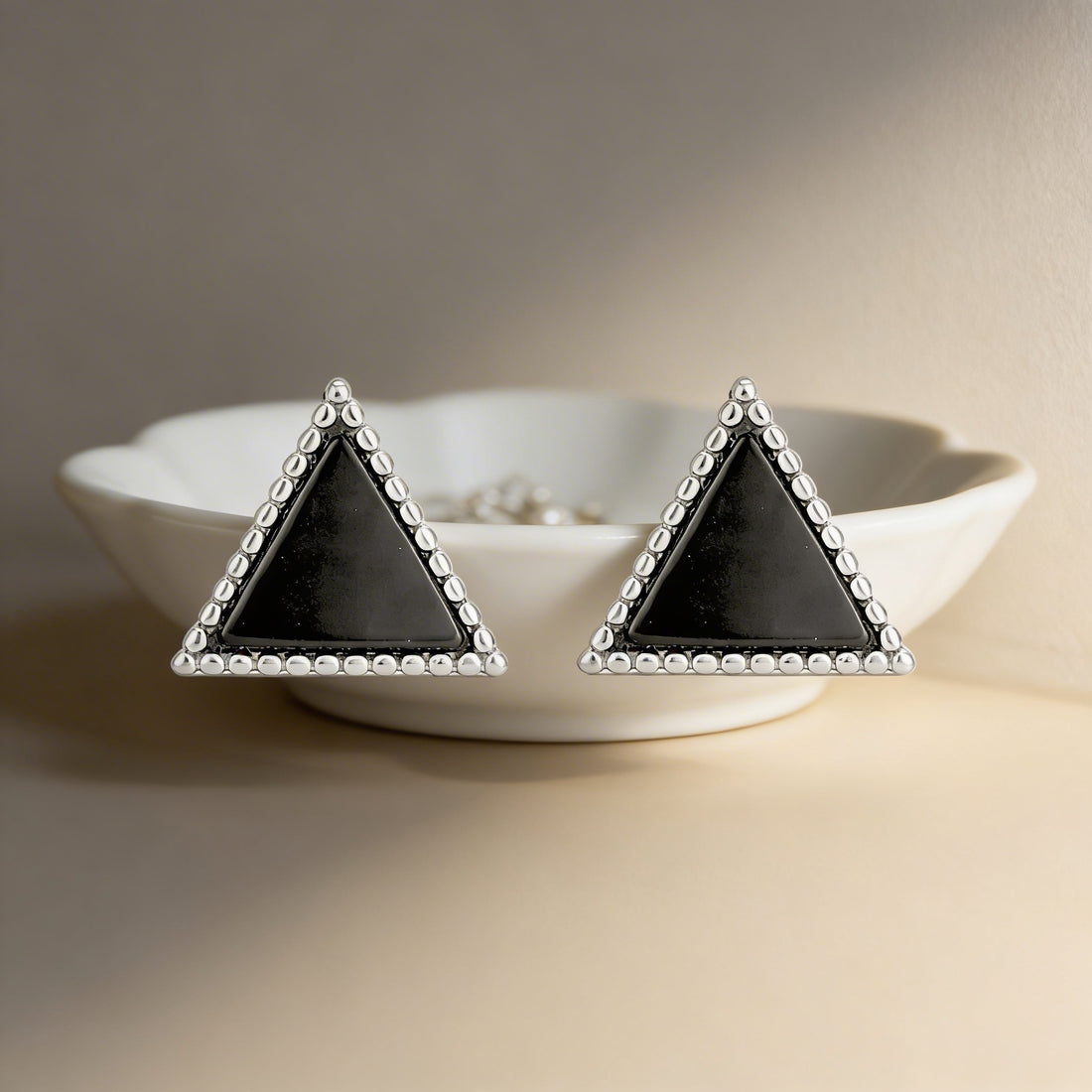 Black triangle-shaped earrings with silver accents on a beige surface.