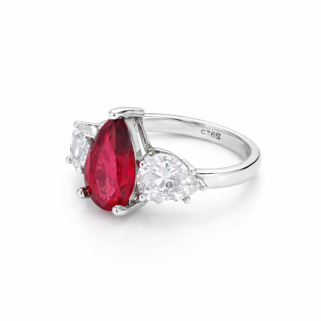 Silver ring with a red gemstone and clear stones on a white background