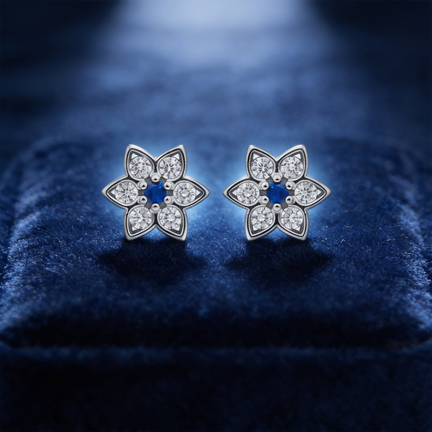 Flower-shaped silver earrings with clear stones on a blue velvet background