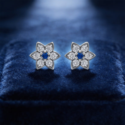Flower-shaped silver earrings with clear stones on a blue velvet background