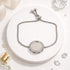 Silver bracelet with a round pendant on a white surface with decorative elements