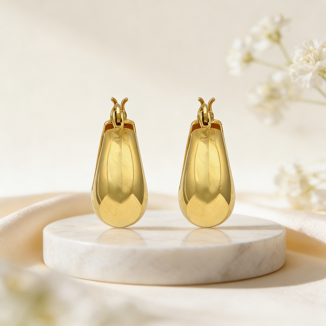 Gold earrings on a marble stand with a soft floral background