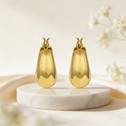 Gold earrings on a marble stand with a soft floral background