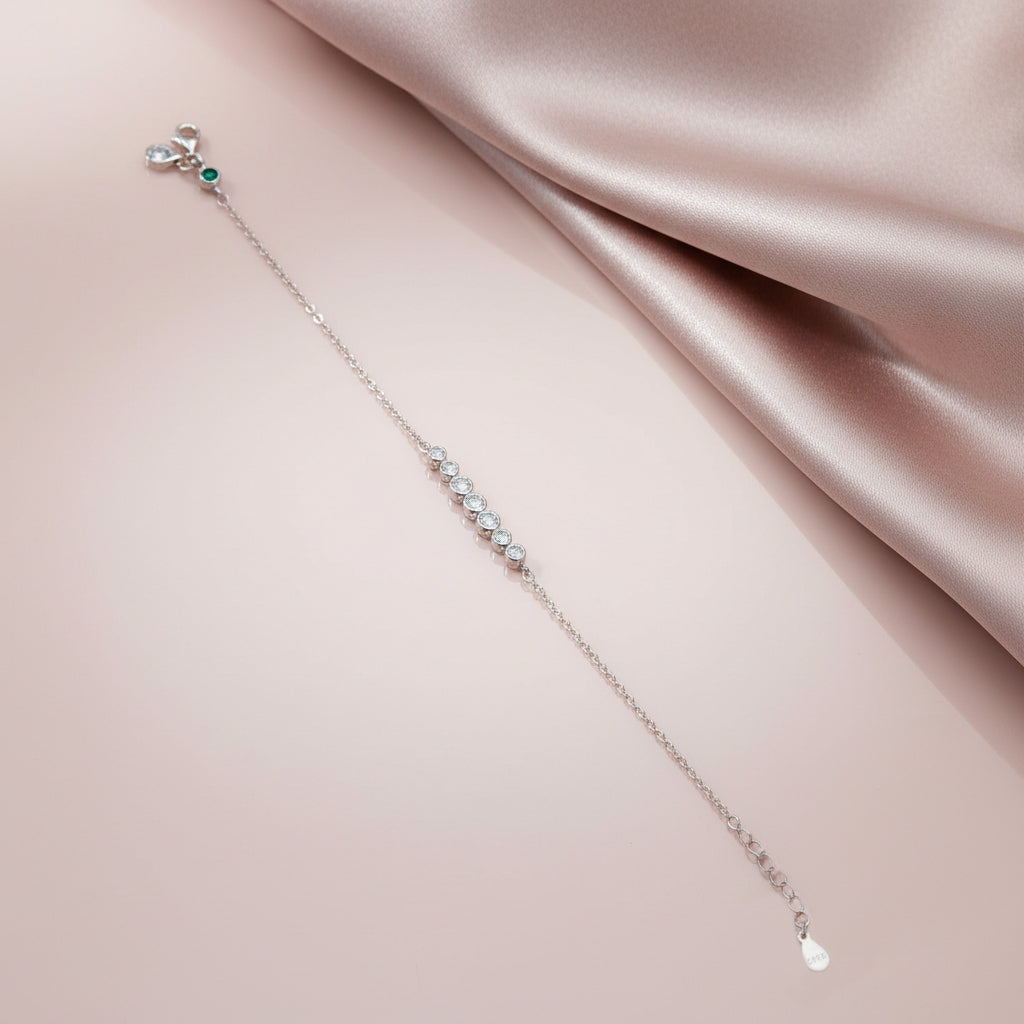 Delicate silver bracelet with small stones on a soft pink fabric background