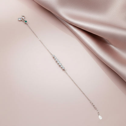 Delicate silver bracelet with small stones on a soft pink fabric background