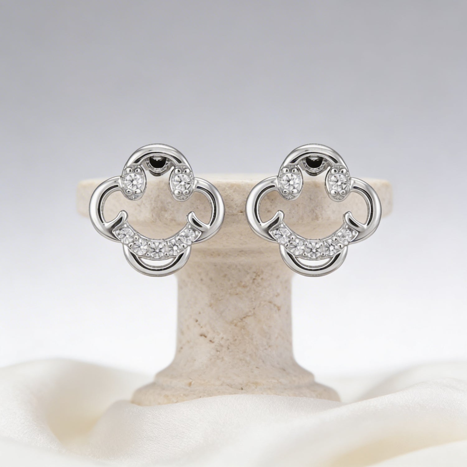 Pair of silver earrings with clear stones on a beige stand against a light gray background