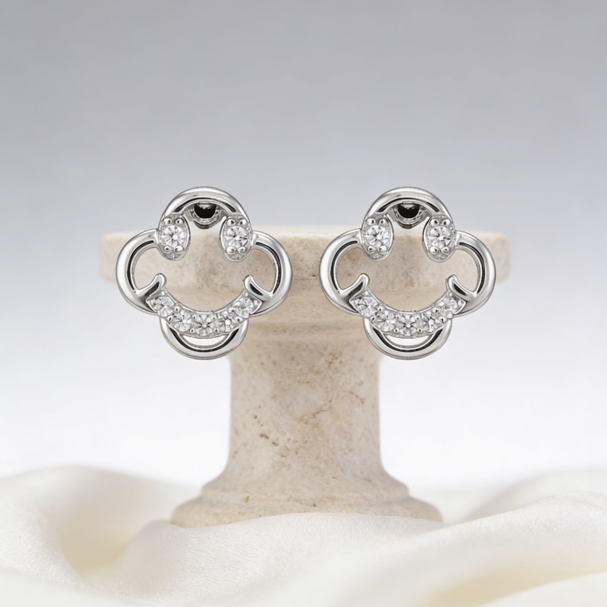 Pair of silver earrings with clear stones on a beige stand against a light gray background