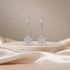 Silver crown-shaped earrings on a beige stone surface with a soft beige background