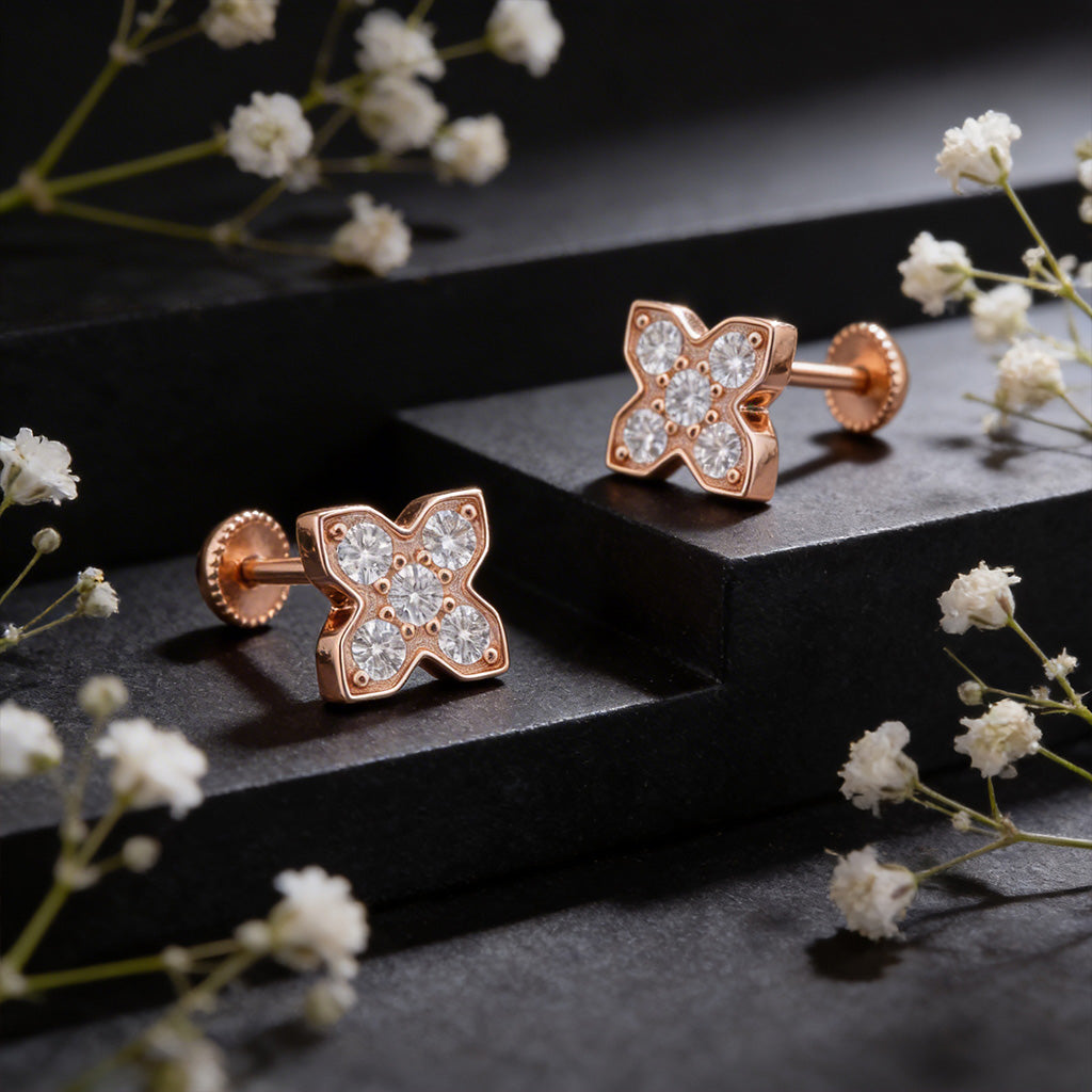 Rose gold earrings with diamond accents on a dark surface with white flowers.