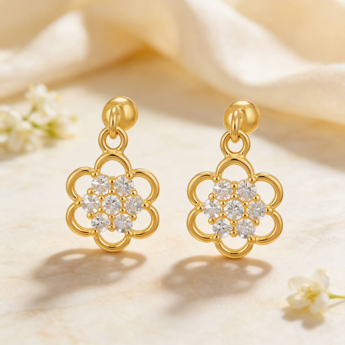 Gold earrings with floral design and clear stones on a soft beige background