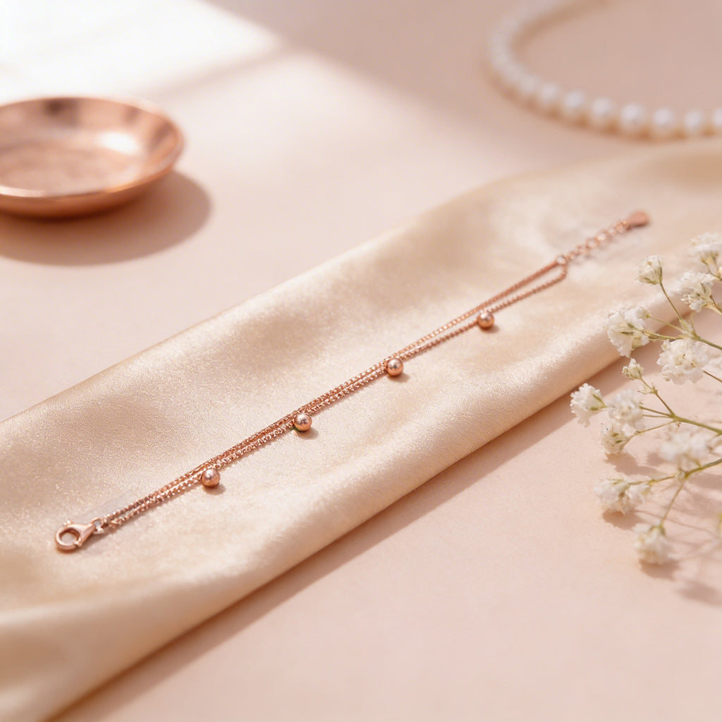 Rose gold bracelet on a beige fabric surface with a pearl necklace and small dish in the background.