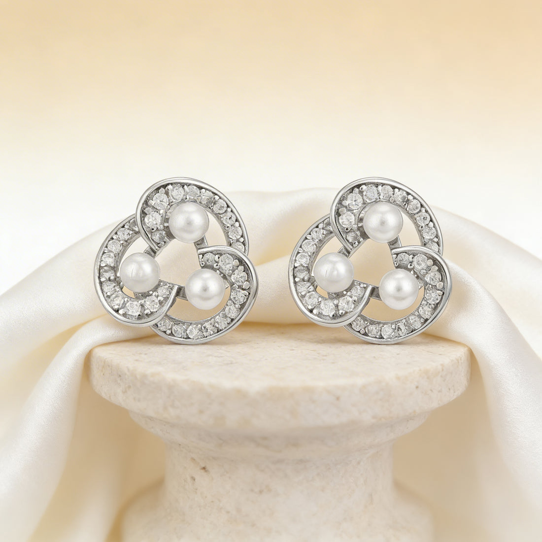 Pair of silver earrings with pearls on a beige fabric background