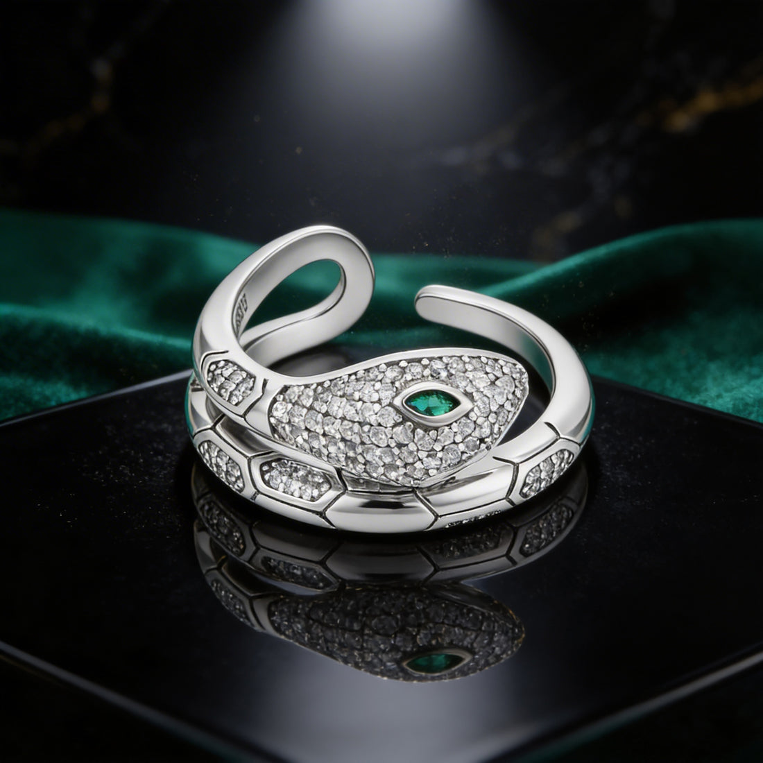 Silver snake-shaped ring with green gemstone on a dark surface