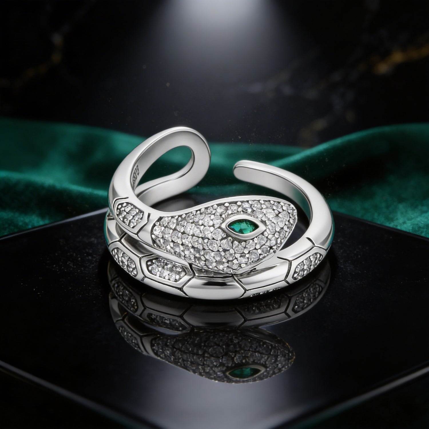 Silver snake-shaped ring with green gemstone on a dark surface