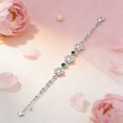 Silver bracelet with green gemstones on a soft pink floral background