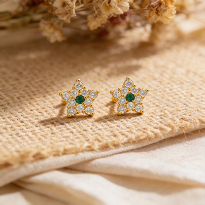 Gold star-shaped earrings with green gemstones on a textured beige surface.