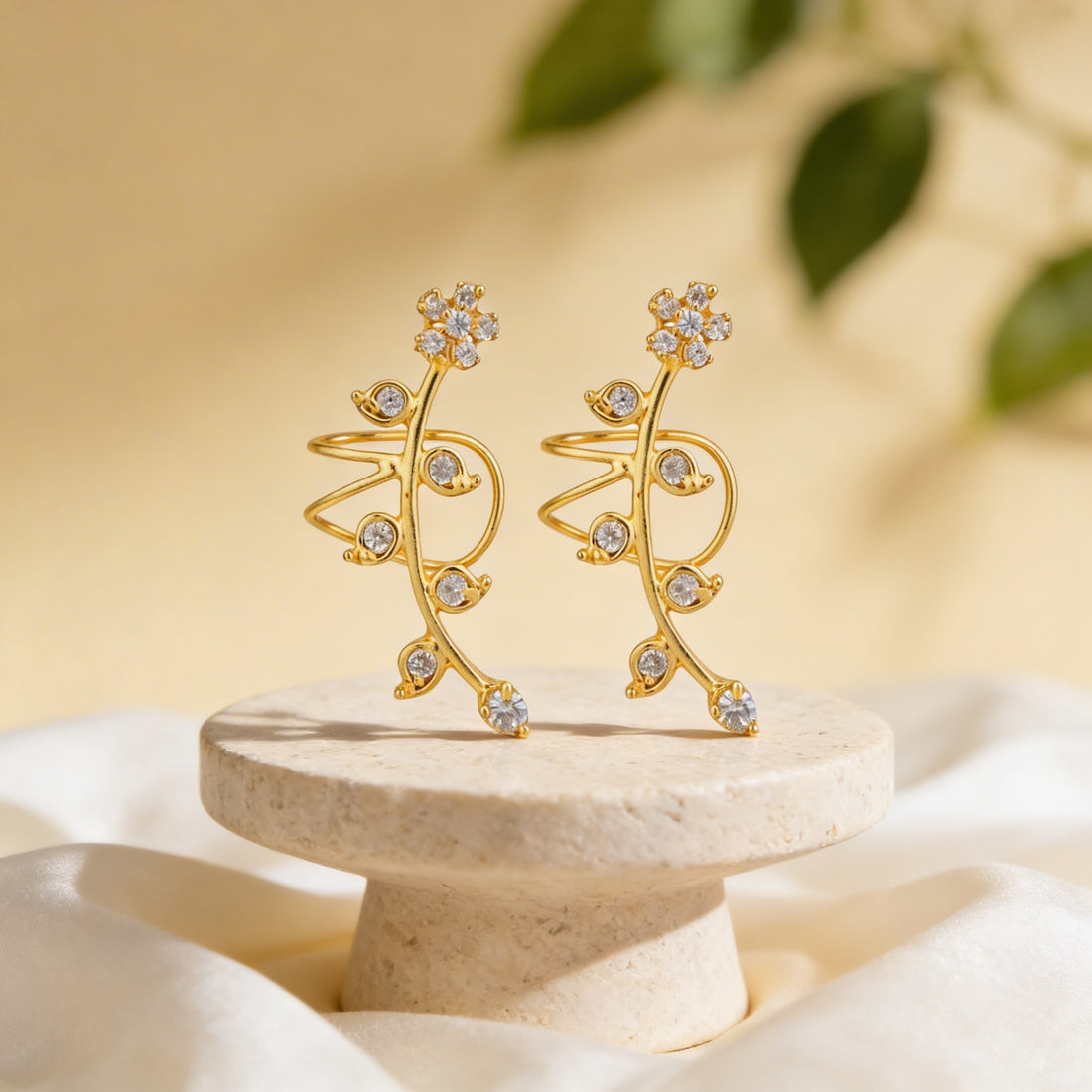 Gold earrings with crystal accents on a beige stand against a blurred natural background
