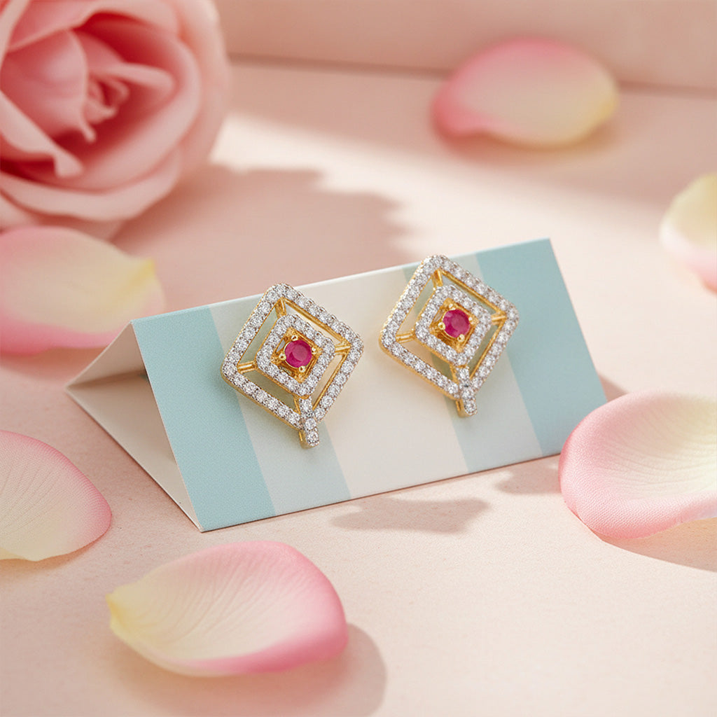 Gold earrings with red gemstones on a card surrounded by pink roses and petals.