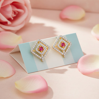 Gold earrings with red gemstones on a card surrounded by pink roses and petals.