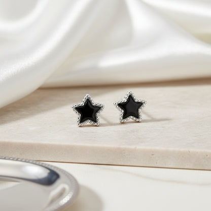 Star-shaped earrings with black stones on a light wooden surface
