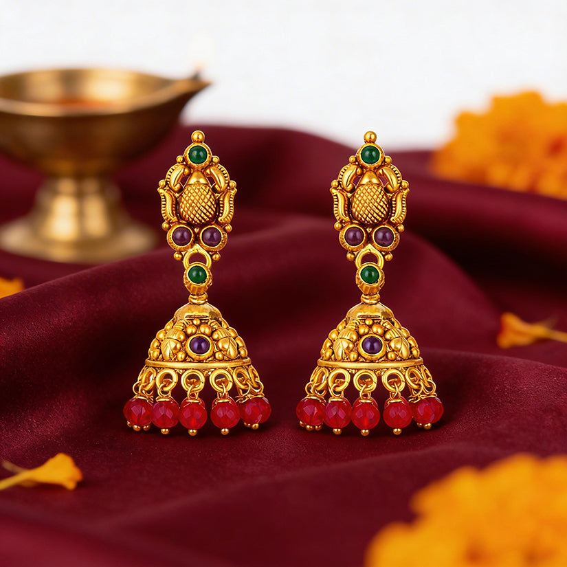 Gold earrings with red and green stones on a maroon fabric background