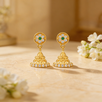 Gold earrings with green and white stones on a beige surface with flowers.