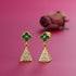 Gold earrings with green and clear gemstones on a pink background
