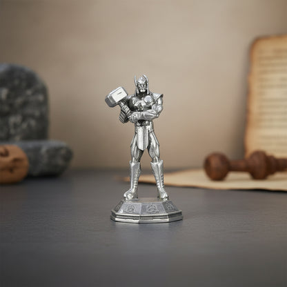 Metallic superhero figurine holding a hammer on a dark surface with a neutral background
