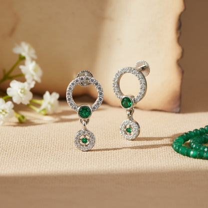 Silver earrings with green gemstones on a beige surface with white flowers.