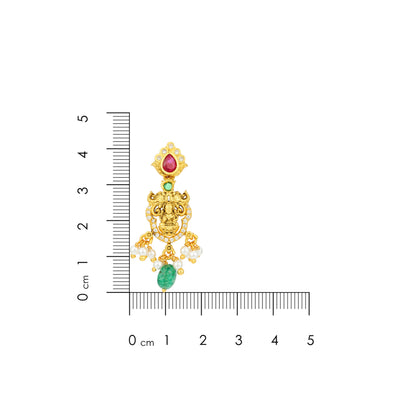 Gold earring with gemstones next to a ruler for scale on a white background