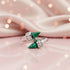 Two silver rings with green gemstones on a pink fabric background