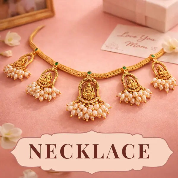 Gold necklace with pendants on a pink surface with flowers and a card.