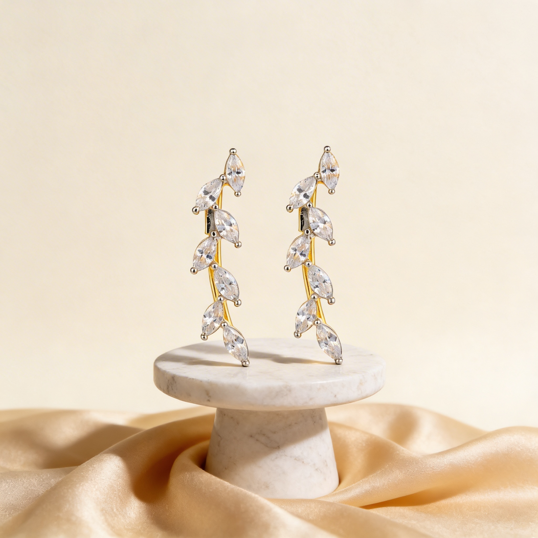 Pair of gold and crystal earrings on a marble stand with a beige background