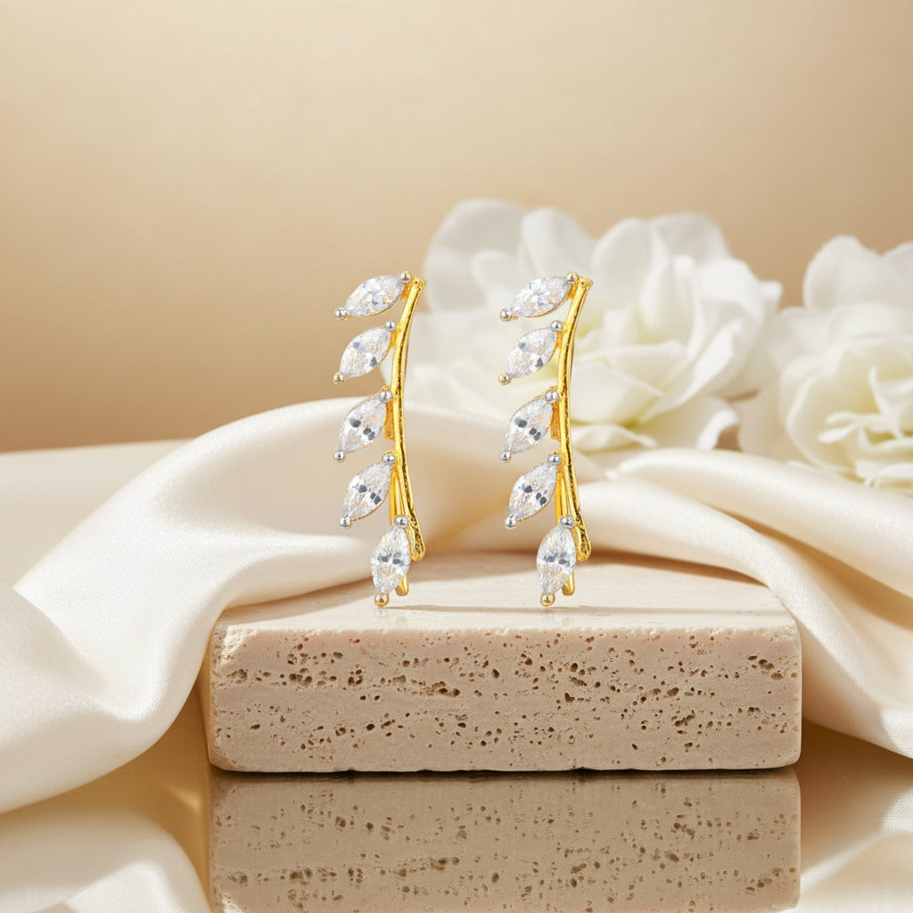 Gold earrings with clear stones on a beige stone surface with white flowers in the background
