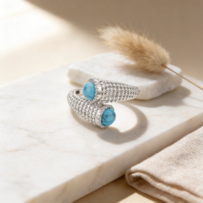Silver ring with turquoise stones on a light wooden surface with a dried plant.