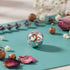 Silver charm with a decorative design on a teal surface with flowers and small pots.