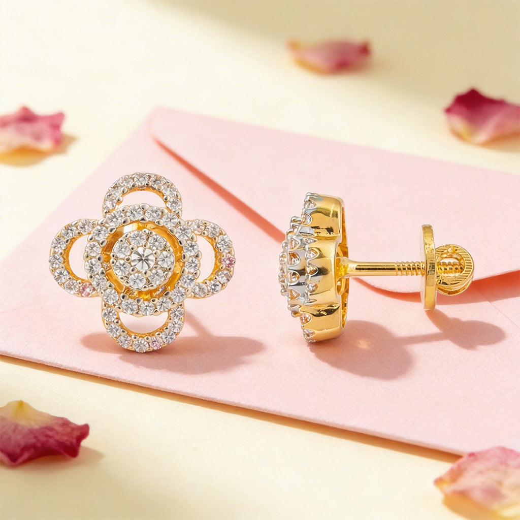 Gold earrings with floral design on a pink surface with flower petals.