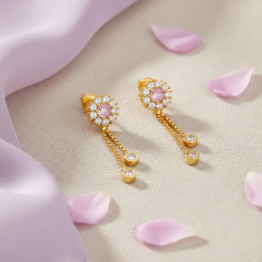 Gold earrings with pink gemstones on a beige surface with pink petals