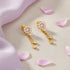 Gold earrings with pink gemstones on a beige surface with pink petals