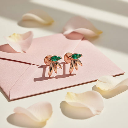 Rose gold earrings with green gemstones on a pink card with flower petals