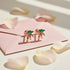 Rose gold earrings with green gemstones on a pink card with flower petals