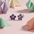 Purple flower-shaped earrings on a pink background with origami decorations