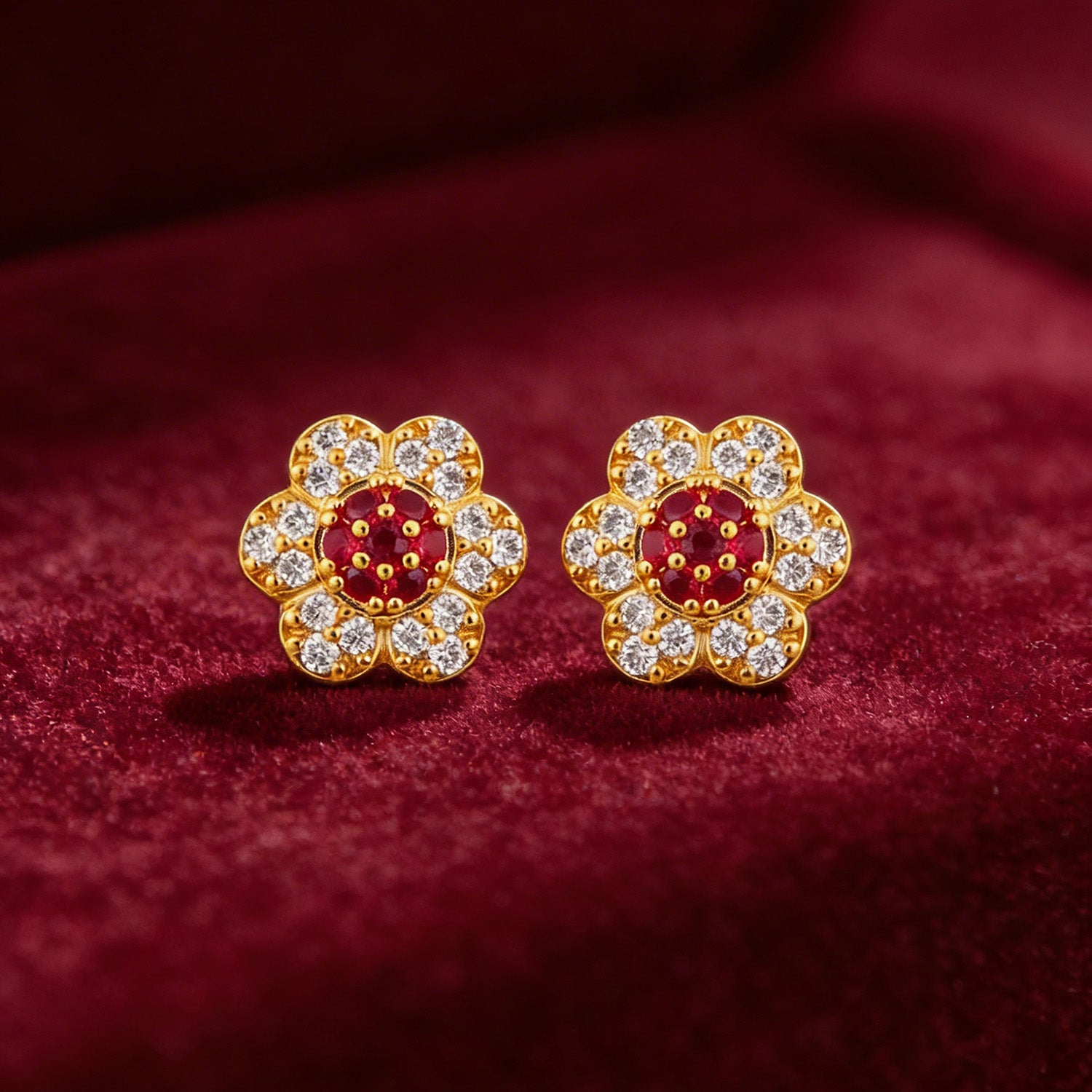 Gold flower-shaped earrings with red and clear gemstones on a red fabric background