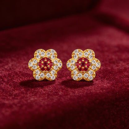 Gold flower-shaped earrings with red and clear gemstones on a red fabric background