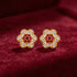 Gold flower-shaped earrings with red and clear gemstones on a red fabric background