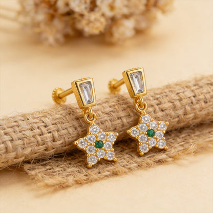 Gold earrings with star designs and gemstones on a textured beige surface