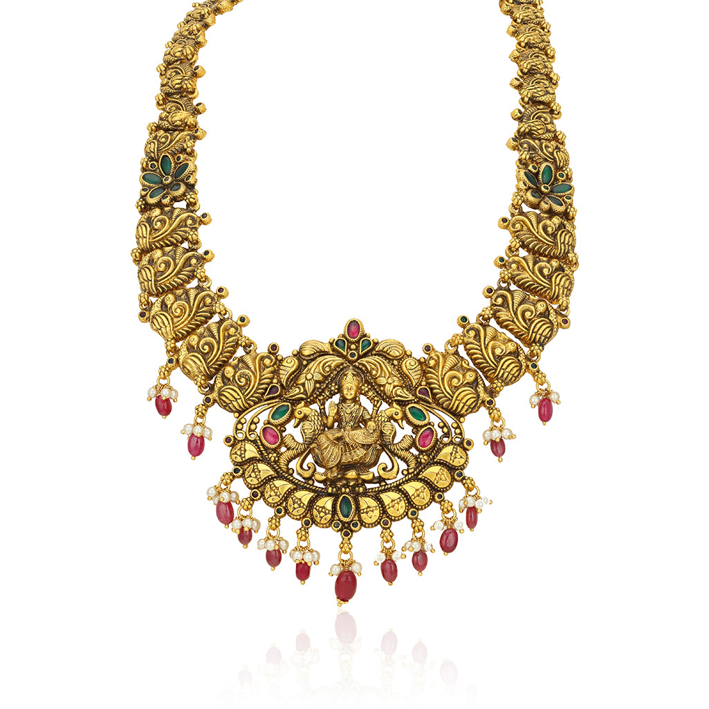 Gold necklace with intricate designs and red and green gemstones on a white background